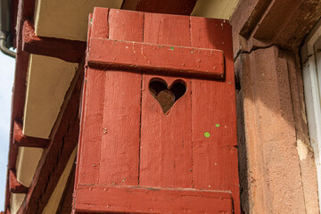 detail of old red wooden shutter with hole in heart shape on half-timbered house in small city in south germany