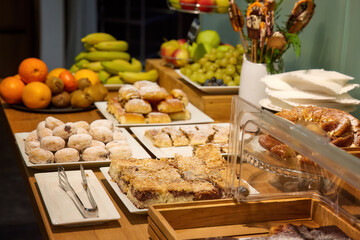 Breakfast in hotel, lighted table with various dishes, fruit and sweet pastries, authentic situation, blurred background. 