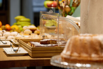 Breakfast in hotel, lighted table with various dishes, fruit and sweet pastries, authentic situation, blurred background. 