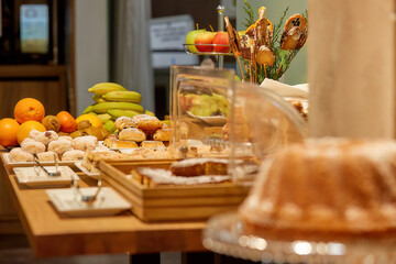Breakfast in hotel theme: table with various dishes, fruit and sweet pastries, authentic situation, blurred background. 