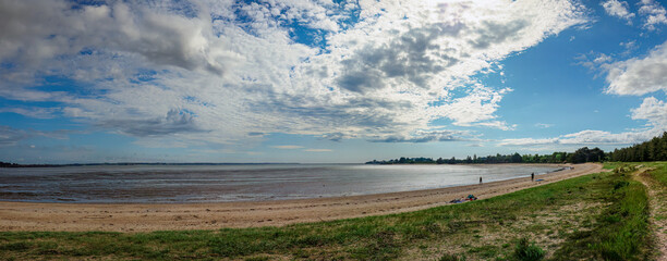 Panorama of a beach edge at low tide, cloudy sky, sand and grass. Penestain, Brittany, France.
