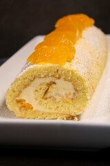 Delicious homemade mandarin cake roll with buttercream feeling, white plate and grey table background