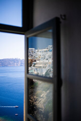 Window scenic view of a coastal landscape in Santorini with white apartment houses reflected in a window glass