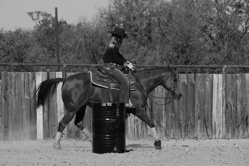 Barrel racing practice for rodeo on western ranch in black and white with cowgirl riding horse...
