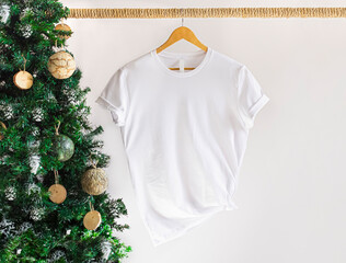 Mockup of white textile tshirt with hanging on a hanger , front view, with christmas tree. 3001 White t shirt mockup with copy space. - obrazy, fototapety, plakaty