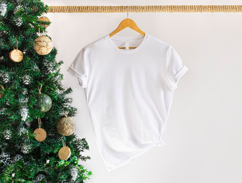 Mockup of white textile tshirt with hanging on a hanger , front view, with christmas tree. 3001 White t shirt mockup with copy space.