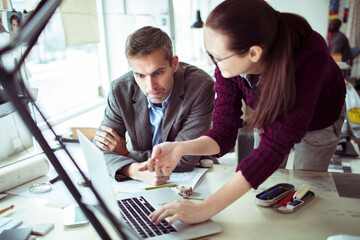 Fototapeta premium Young man and woman using the laptop while working together on a project in a startup company office