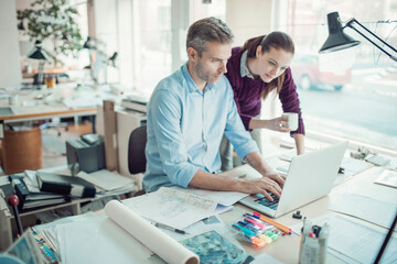 Fototapeta premium Young man and woman using the laptop while working together on a project in a startup company office