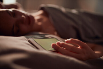 Young woman sleeping in her bed while holding a smartphone with a blank screen