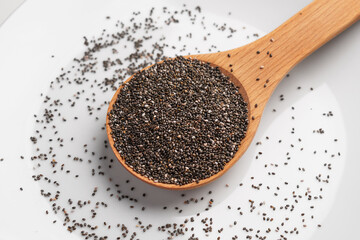 Healthy raw chia seeds in a wooden spoon on white ceramic surface