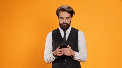 Competent waiter checks smartphone, ready to serve clients at table. Sophisticated, trendy staff...