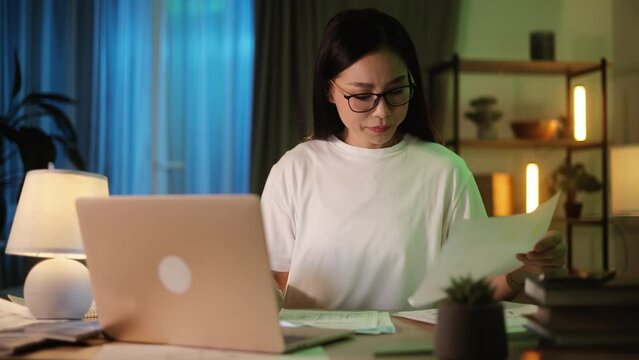 Nervous sad young asian woman freelancer or teacher having problem with distance remote paperwork paper presentation graphs statistics and looking at camera at home Stress work at late night concept