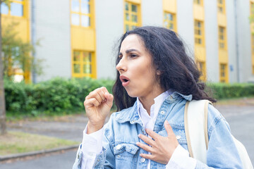 Woman on the street on the background a hospital or educational institution experiences a coughing...