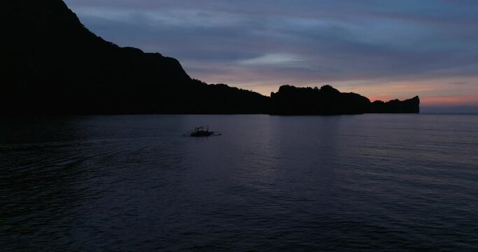 Sunset drone view above the sea, following a traditional boat, Coron, Philippines