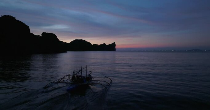 Sunset drone view above the sea, following a traditional boat, Coron, Philippines