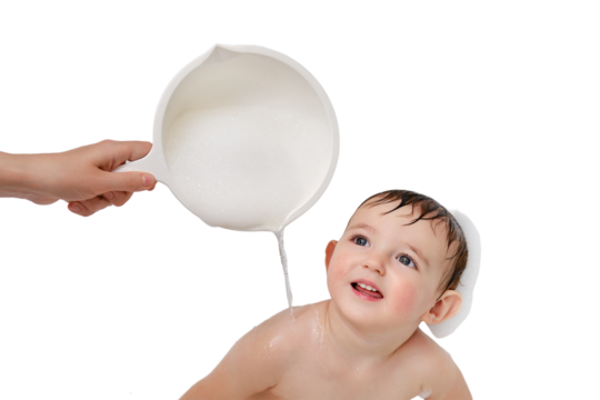 A mother washes a child sitting with soap, isolated on a white background. Mom hand waters the baby from a ladle in bath. Kid aged one year and three months