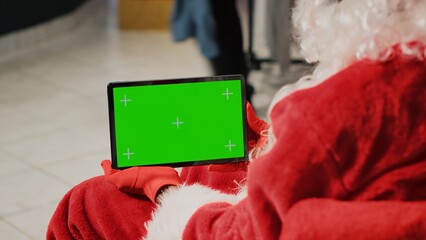 Employee in xmas ornate clothing store dressed as Santa Claus holding green screen tablet, setting up website clothing articles, inputting promotional Christmas offers online - Powered by Adobe