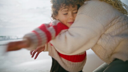 Playful boy running mother on ocean shore. Happy parent woman hug spinning child