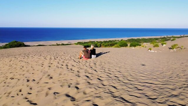 Circular flight of drone, aerial photography of girl or man of couple sitting on sand dunes on beautiful beach of Patara on Mediterranean coast. Wanderlust, looking into distance at sea and mountains.