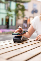 Close up from hands of young woman paying with her smart phone, NFC technology concept