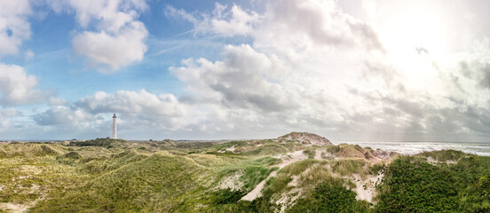 Landscape panorama with a view of a lighthouse and the coast of Denmark in the town of Hvide Sande with the Lyngvig lighthouse. Dunes by the sea and strong wind with sunshine. Vacation destination 