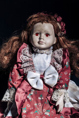 Old dirty porcelain doll with scary red eyes on a dark background. Halloween concept