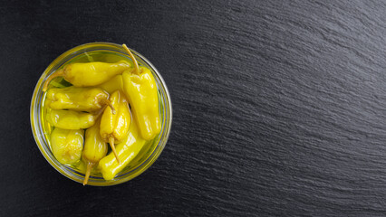 Pickled yellow pepper, pepperoncini or friggitelli in bowl on black background, copy space. Hot pepper marinated, brined. Traditional Italian and greek cuisine, ingredient for salad, pasta, sauce.