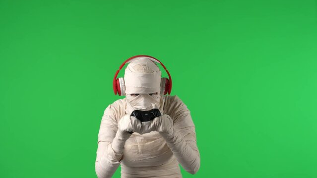 Green screen isolated chroma key video capturing a mummy wearing headphones and holding a gamepad like it's playing a videogame.