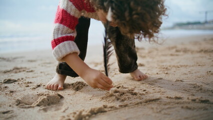 Little boy drawing sand with bird feather closeup. Focused kid resting beach