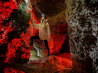 Girl with flashlight explores dark creepy abandoned underground limestone cave - obrazy, fototapety, plakaty