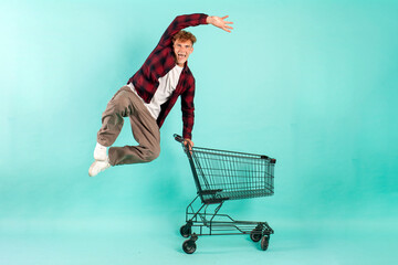 young crazy guy shopper jumps and rejoices with shopping cart from supermarket © Богдан Маліцький