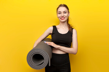 young sports girl in sportswear with yoga mat smiles on yellow isolated background, woman goes to do fitness