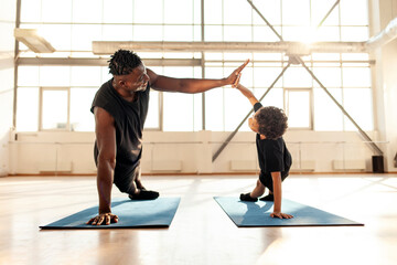 African-American boy doing exercises on yoga mat and doing push-ups with his dad, man training his...
