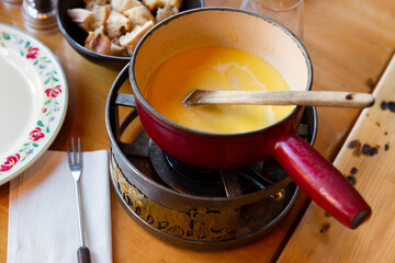 Fondue Savoyarde, melted cheese dish, heating in caquelon on table.