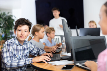 Boy student learning to use computer in group in classroom