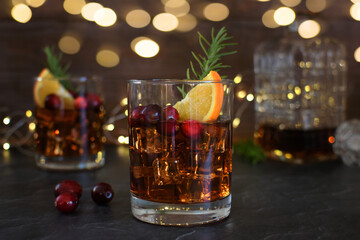Festive winter holiday cocktail garnished with rosemary, cranberries and orange slice with bokeh lights