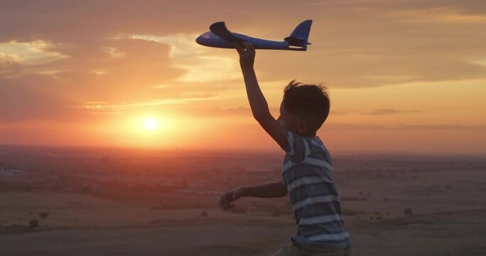 Kid boy runs jumps with a toy airplane at beautiful sunset. Kid dream. Happy childhood. Silhouette shot