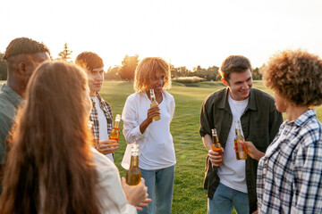 group of multiracial young people holding bottles of beer and talking at outdoor party