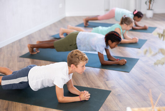 preteen girls and boys together in yoga pose upward-facing dog at gym