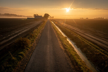 Aerial view of a beautiful sunrise on a rural farmland road. Skagit Valley is the agricultural hub of western Washington state. Historic barns, irrigation canals and plowed fields dominate the area. 