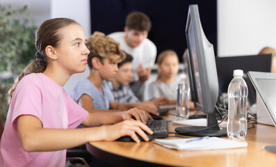 Minor female student sitting at computer together with other attendees of IT courses