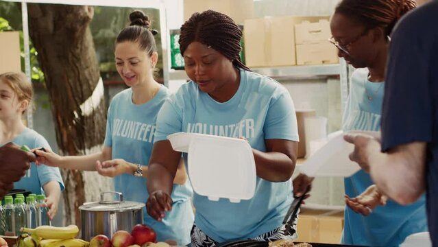 At outdoor food bank, multiethnic female volunteers provide free food to homeless men. Voluntary ladies provide humanitarian relief and create community by assisting the hungry and underprivileged.