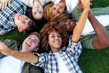 group of multiracial young people relax and lie together on grass in the park and smile, team of interracial students