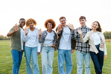 group of multiracial young people standing together and hugging in the park and waving hello