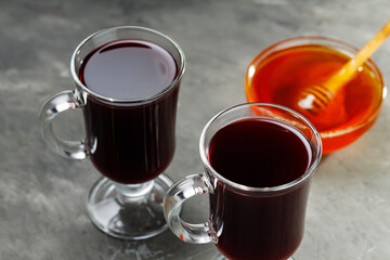 Two glasses of hot mulled wine with honey and spices on dark concrete background. Seasonal mulled drink