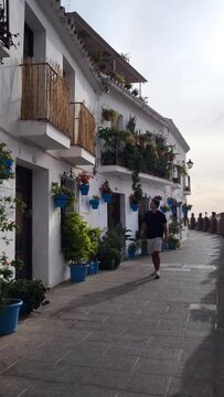 Young tourist man visting typical spanish white town. Street decorated with plants and flowepots. Slow motion.