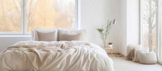 Soft comfortable bed with pillows and blanket by windows in contemporary light bedroom