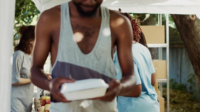 Young African American and Caucasian volunteers handing out free food and necessities to the less poor. At a homeless shelter, friendly charity workers give hunger relief and humanitarian help.