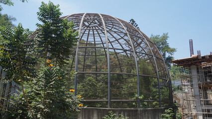 Large metal dome aviary for bird conservation next to a building construction site where crane...
