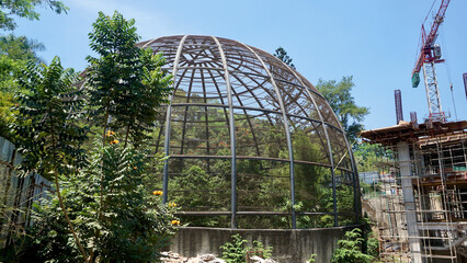 Large metal dome aviary for bird conservation next to a building construction site where crane stand there